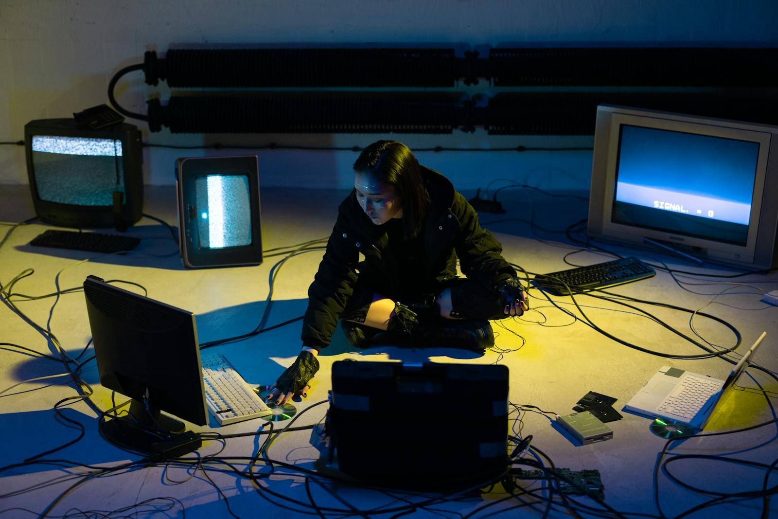 A futuristic hacker sits among vintage monitors and tangled cables, embodying a cyberpunk aesthetic.